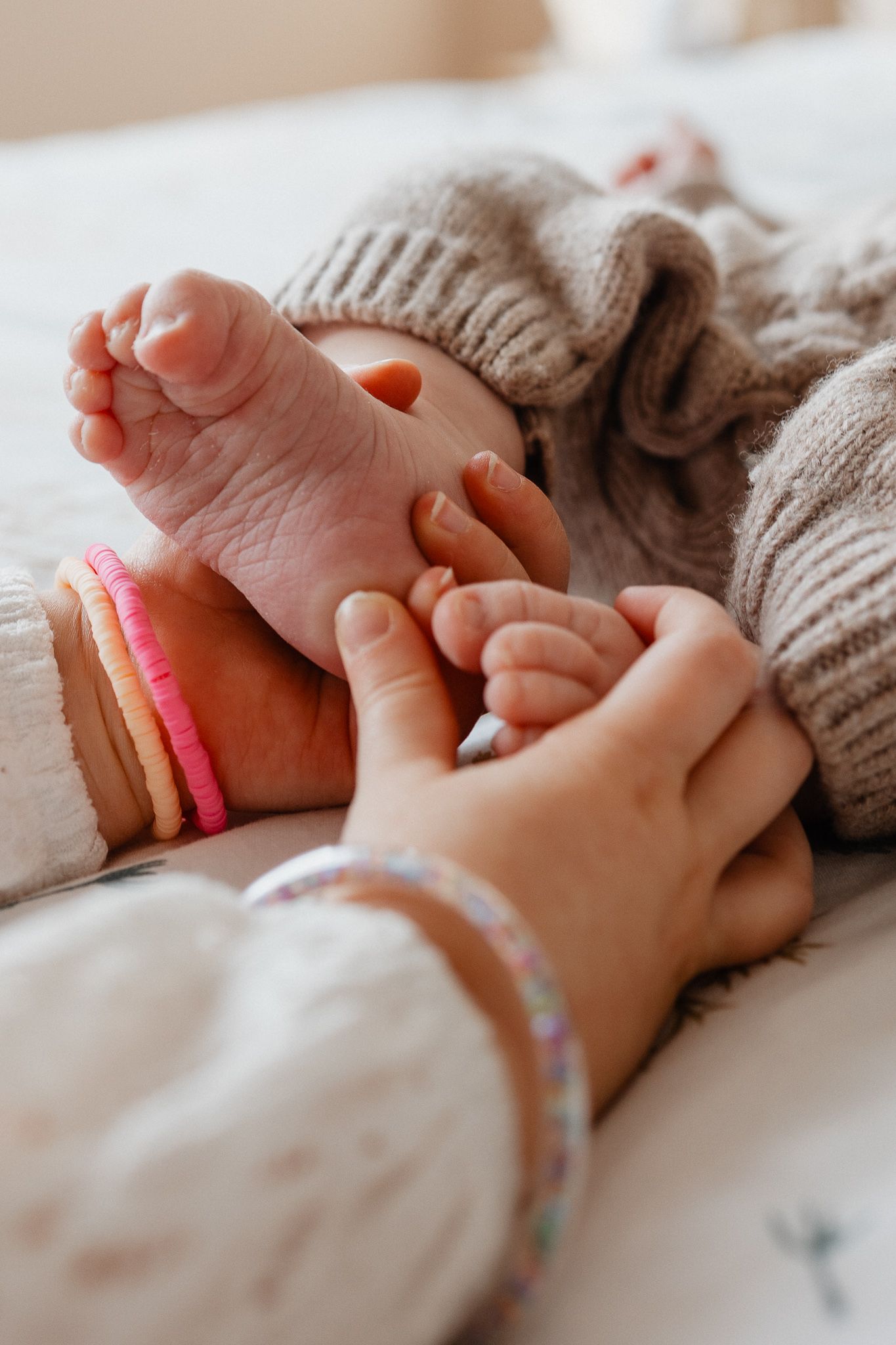 Grande soeur tient les pieds de sa petite soeur pour compter ses orteils, un moment authentique capture par une photographe a Lille
