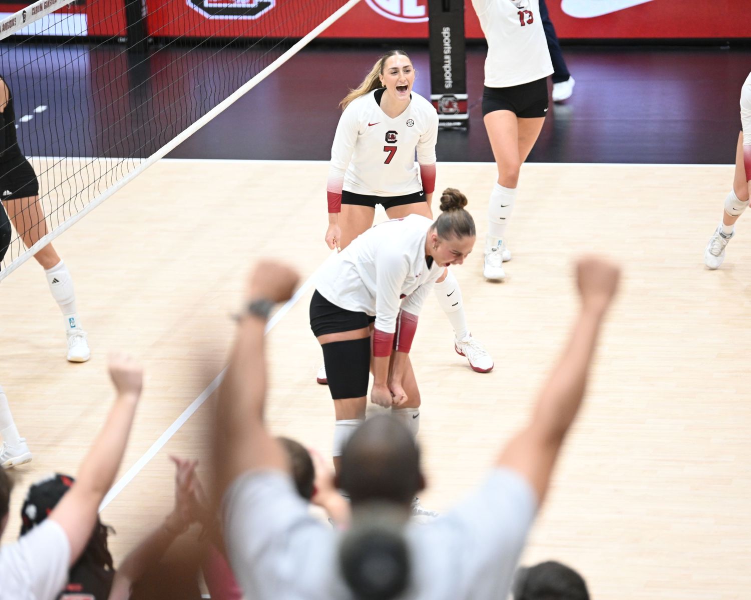 South Carolina volleyball player bends forward as teammates and fans celebrate behind her.