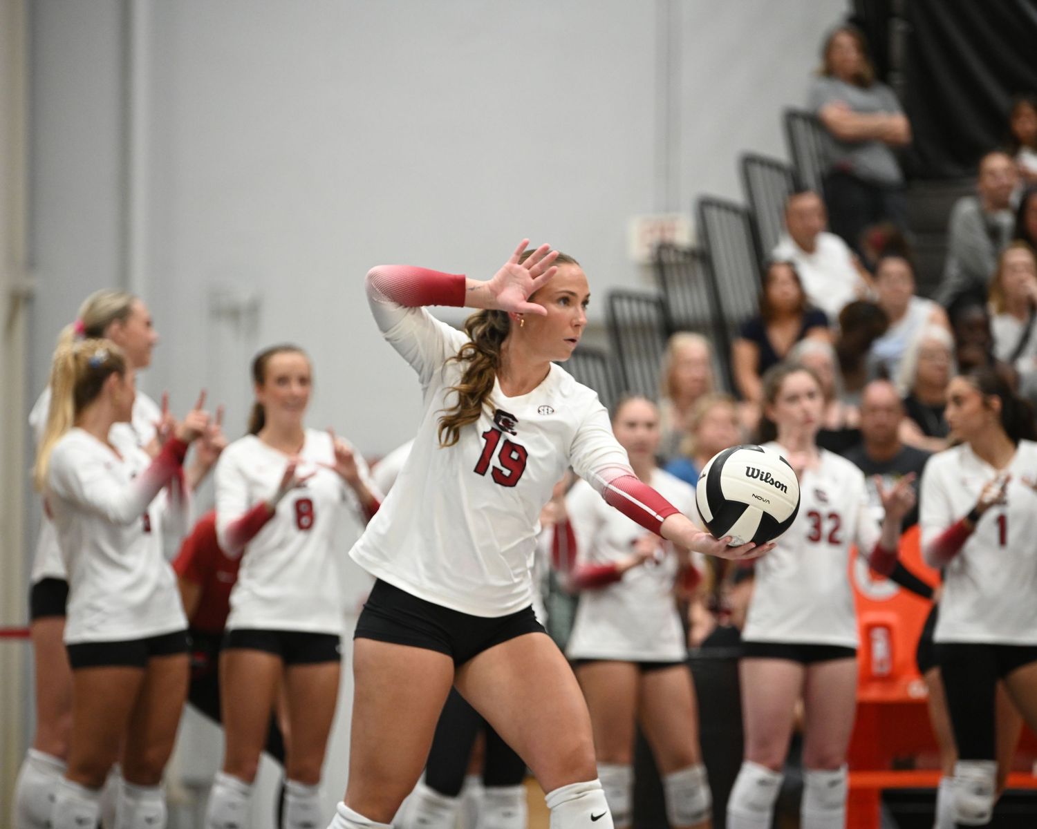 South Carolina volleyball player wearing number 13 prepares to serve as teammates watch.