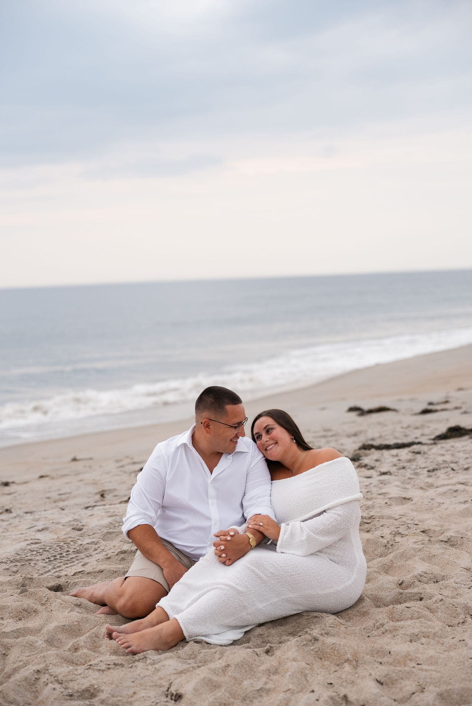 Couple relaxing on sandy beach during sunset engagement photo session.