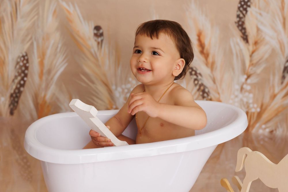 A series of four photos showing a baby playing and splashing in a bathtub during a milk bath photo session.