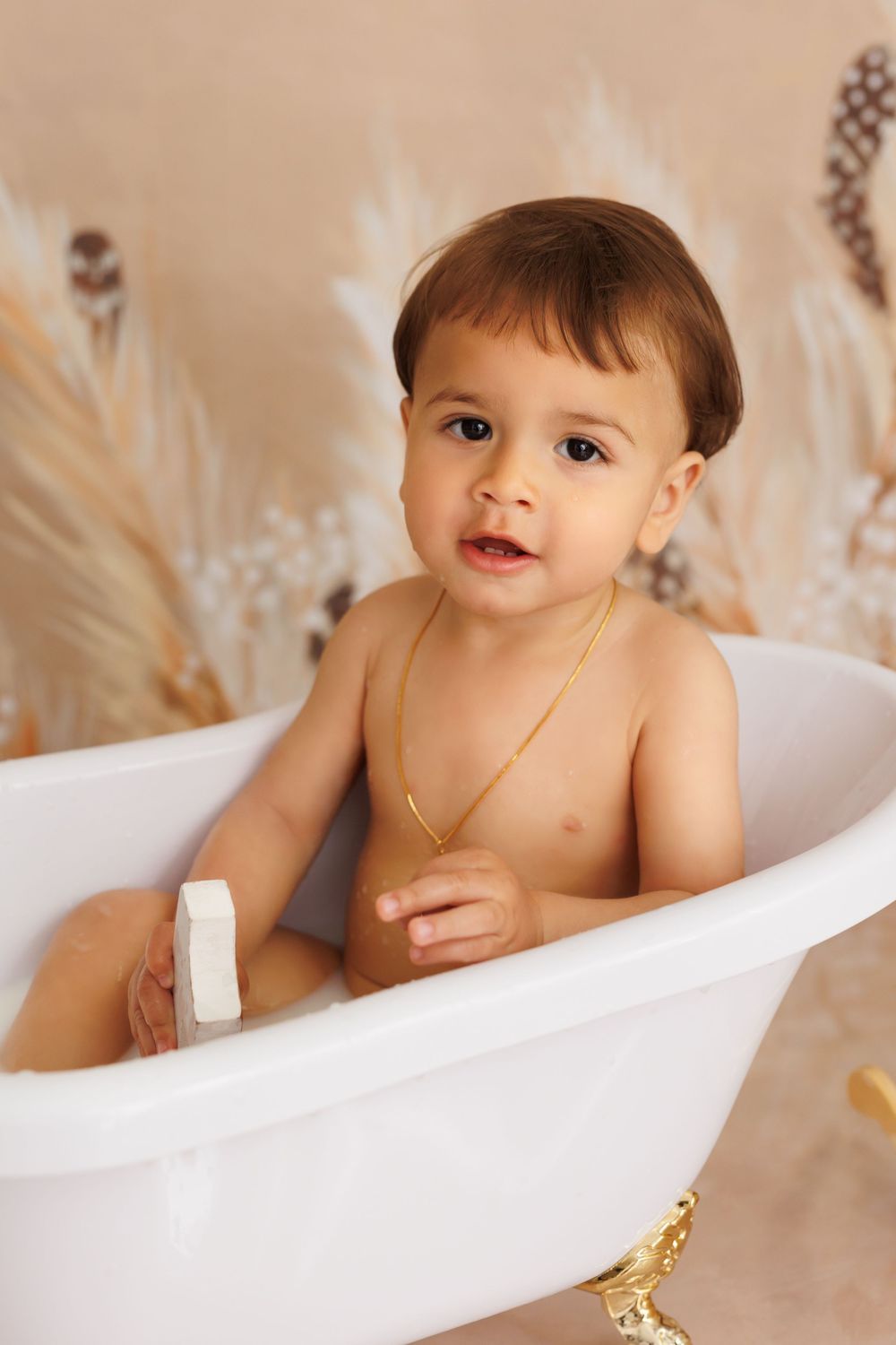 A small child smiles while sitting in a white bathtub during a portrait photography session.