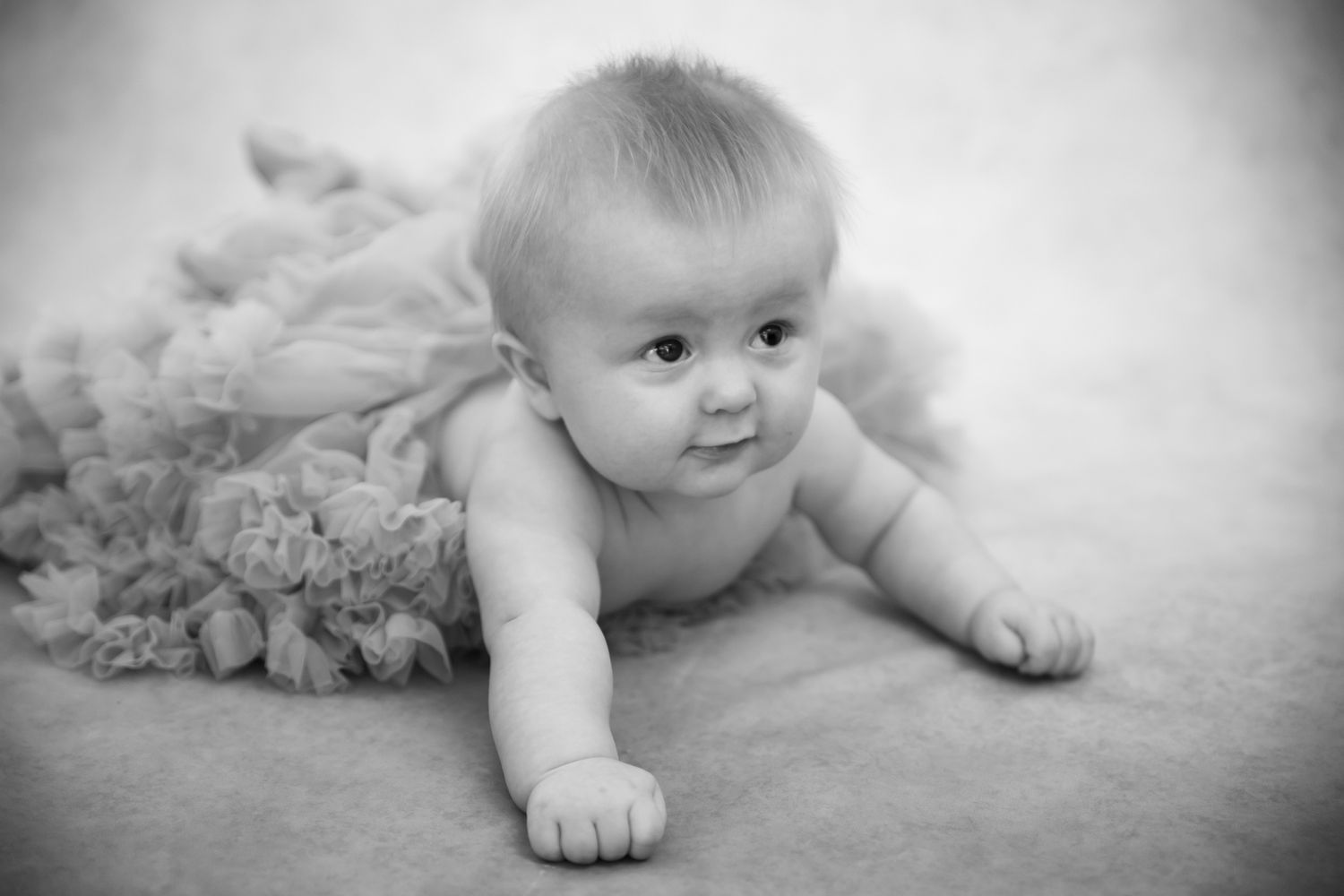 A baby in black and white photography lies on their tummy on a soft textured surface.