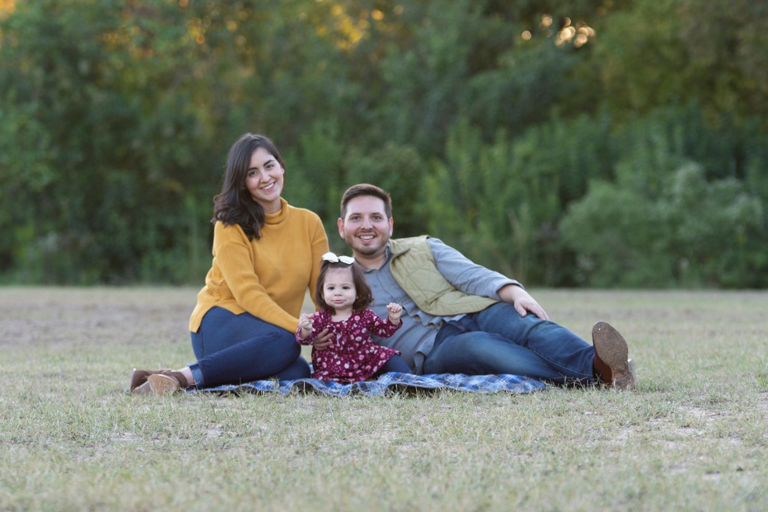 Family of three sitting together on a blanket at Memorial Park, warm natural moment.