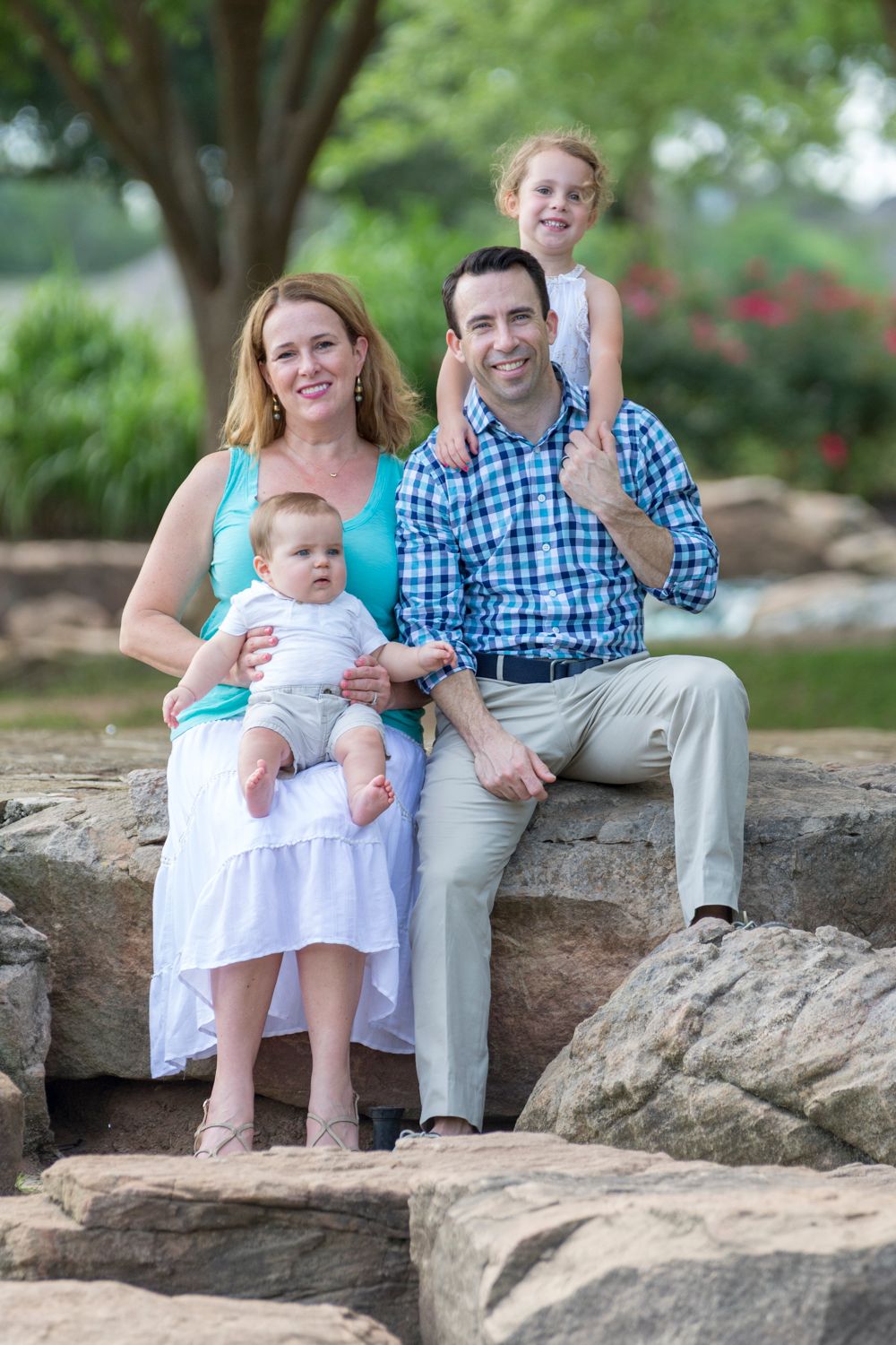 Family of four sitting on rocks at a park, laughing together in natural light.