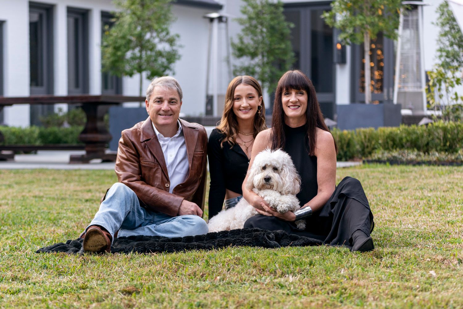 Family of three sitting together on a blanket in their backyard, warm natural moment.