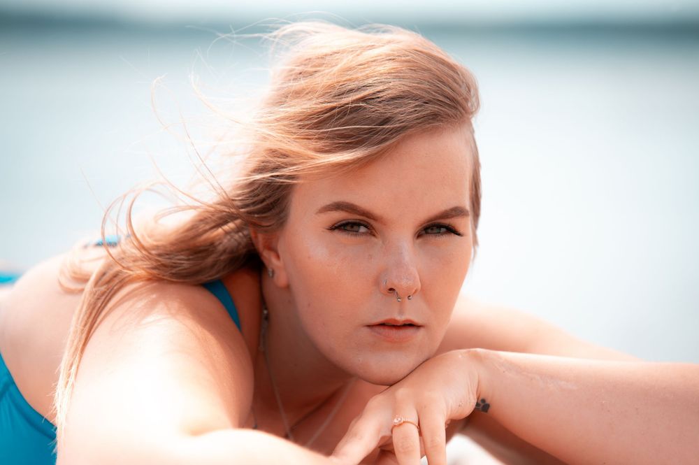 Close-up portrait of blonde woman in blue swimsuit relaxing by the water on sunny day.