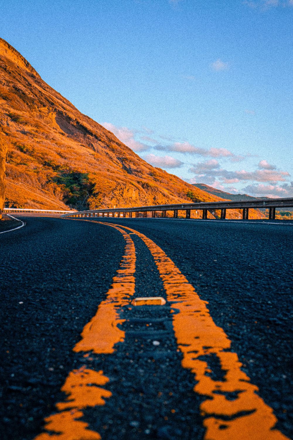 Low angle view of a winding road with yellow center lines beside a golden mountain.