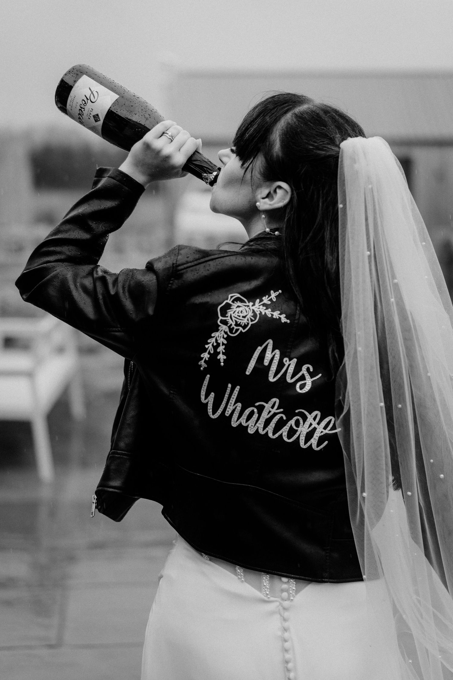 A sequence of black and white photos showing a bride in a wedding dress wearing a custom jacket and drinking from a bottle.