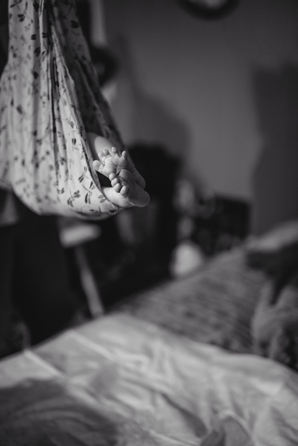 Black and white photo of a newborn baby's tiny feet peeking out from a floral swaddle blanket.