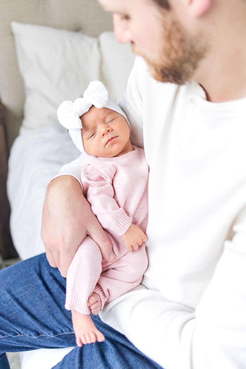Father gently cradling his newborn baby dressed in pink during a bright, natural lifestyle newborn photography session.