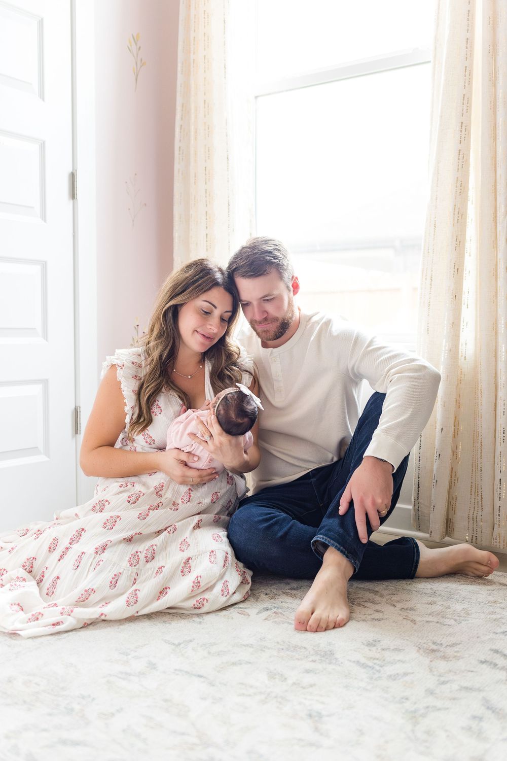 Mother and father sitting together on the floor with their young child during a cozy indoor family photography session.