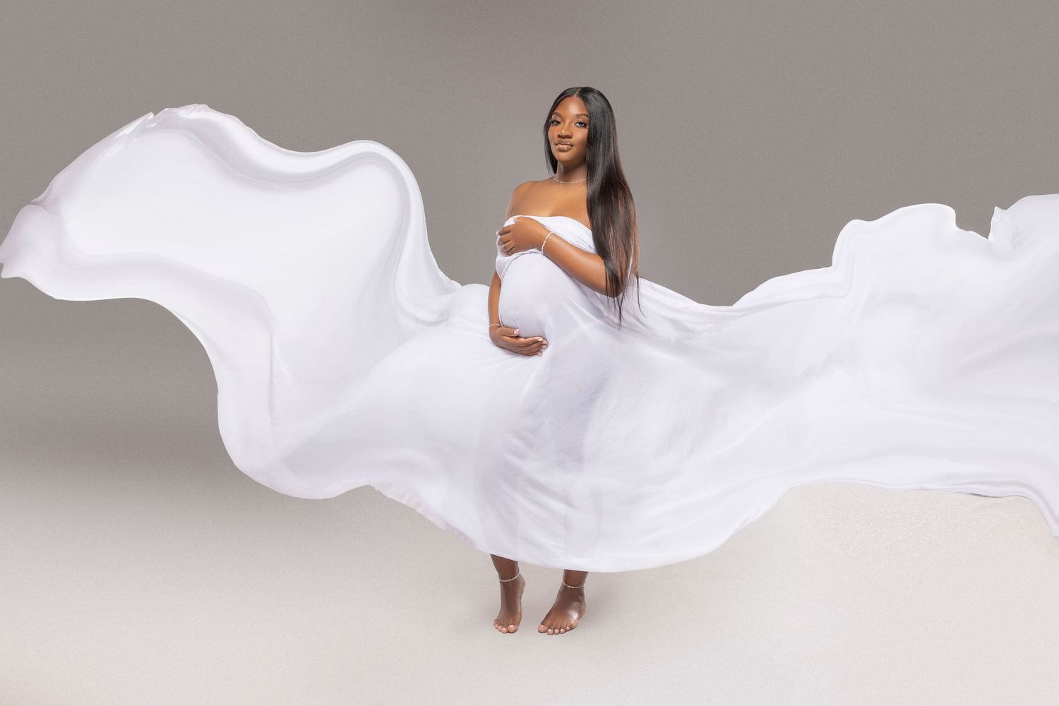 Maternity photo of a woman in flowing white fabric against neutral background.