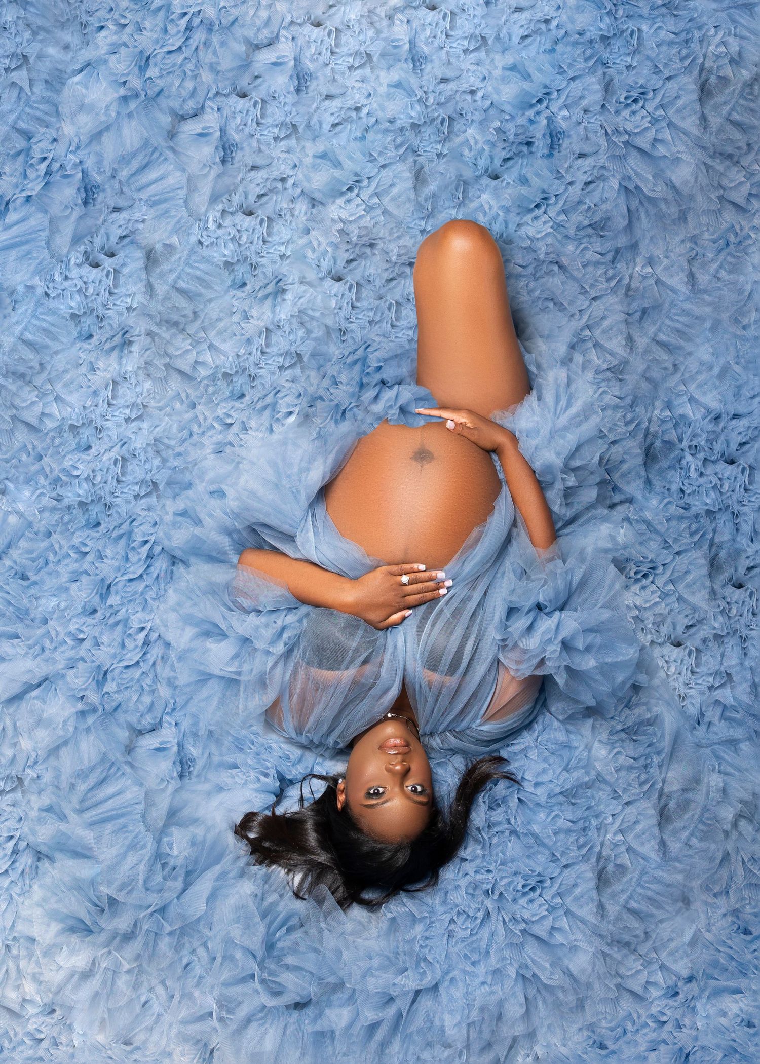 Maternity portrait in blue fabric against textured light blue background.