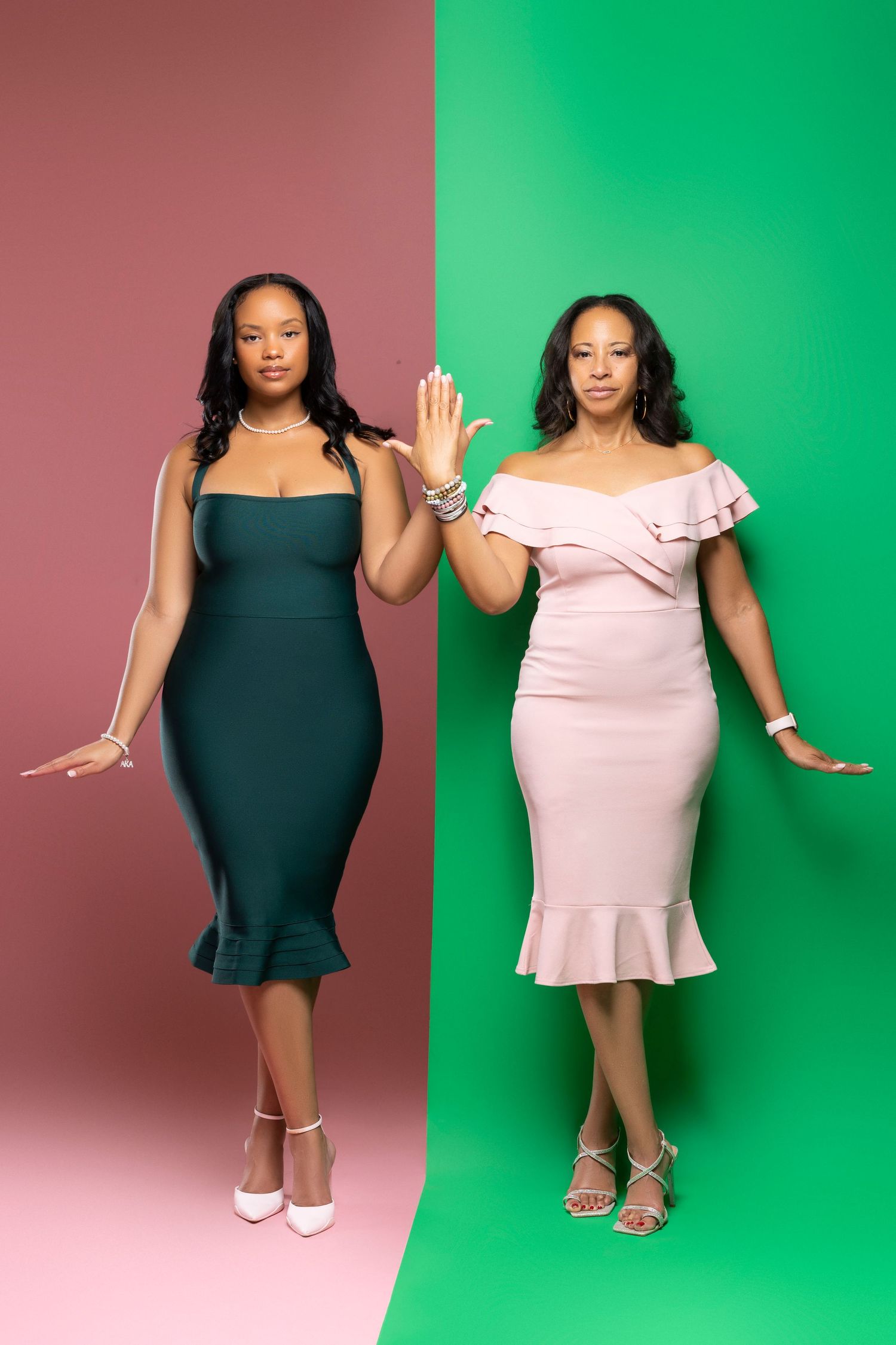 Two women posing in fitted dresses against contrasting pink and green backdrops.