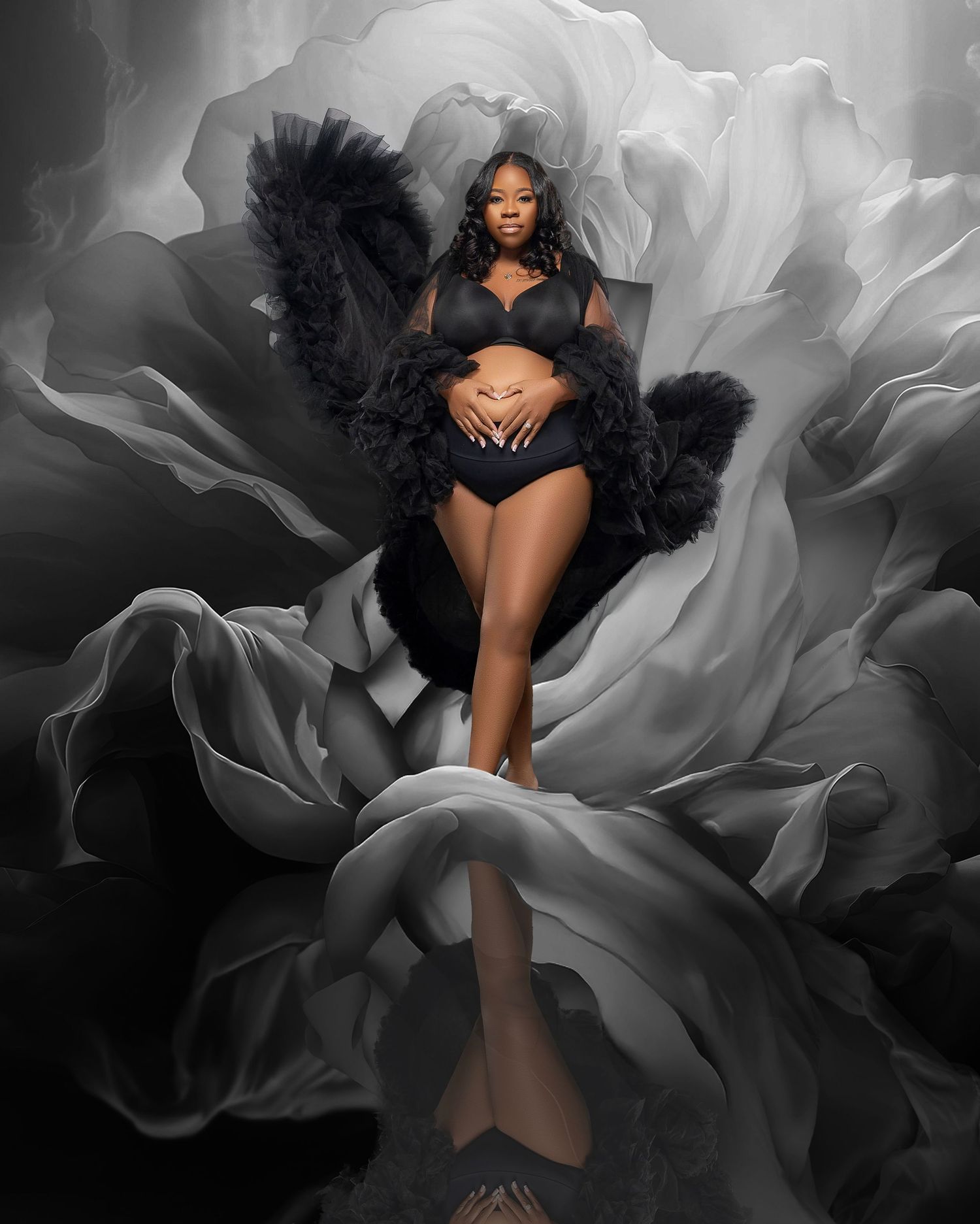 Artistic maternity photo with black lingerie and feathers against dramatic black and white floral background.