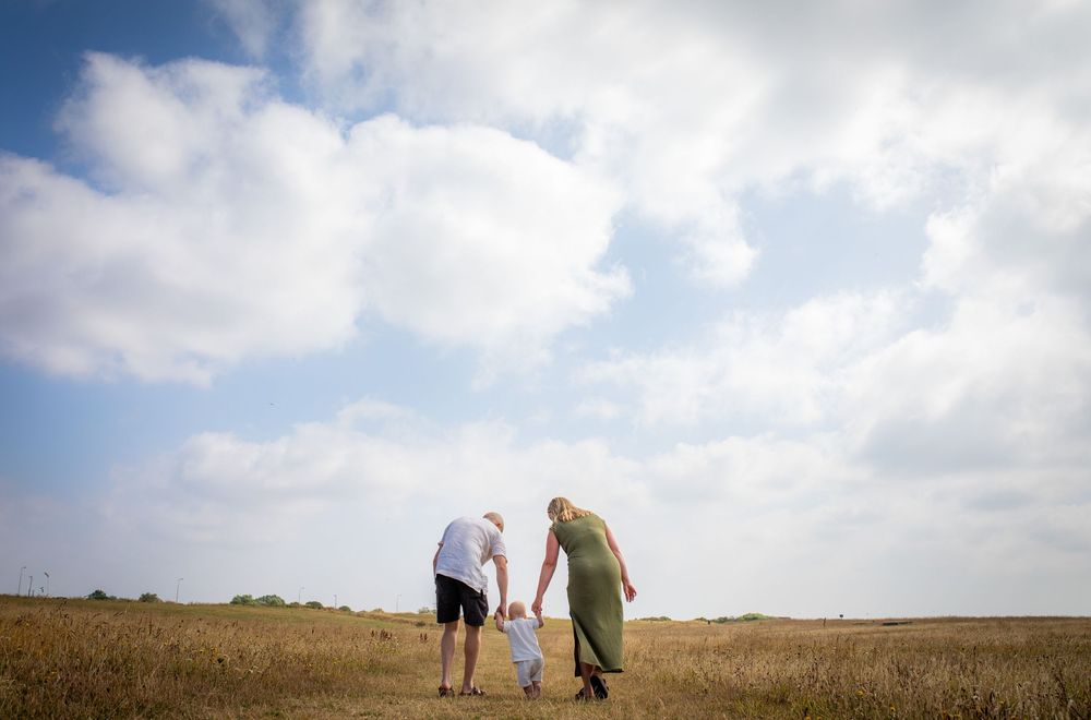 Family walking together through scenic countryside under cloudy sky.