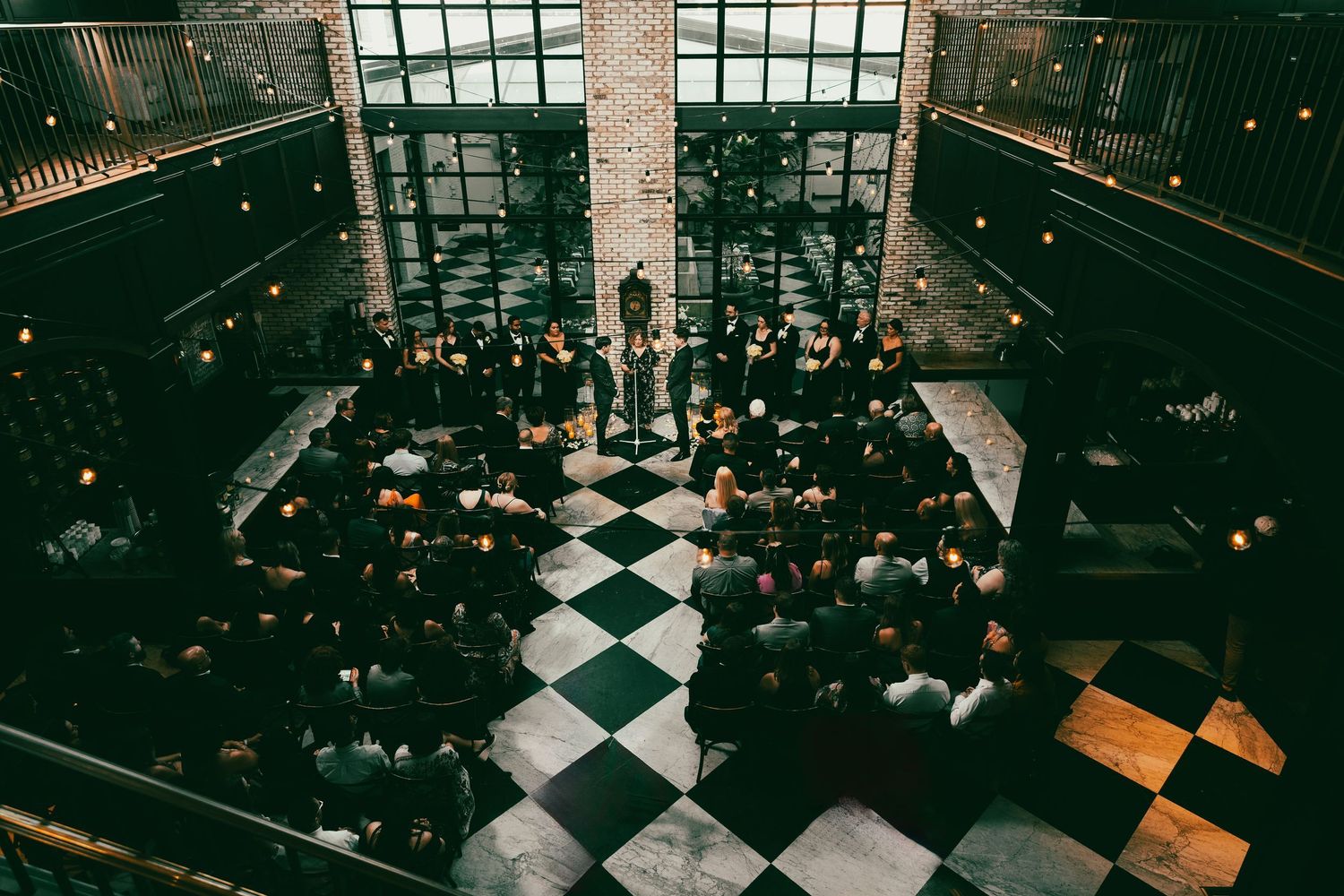 Wide angle photograph of a wedding ceremony inside the Oxford Exchange in Tampa, Florida, featuring dramatic black and white checkered floor