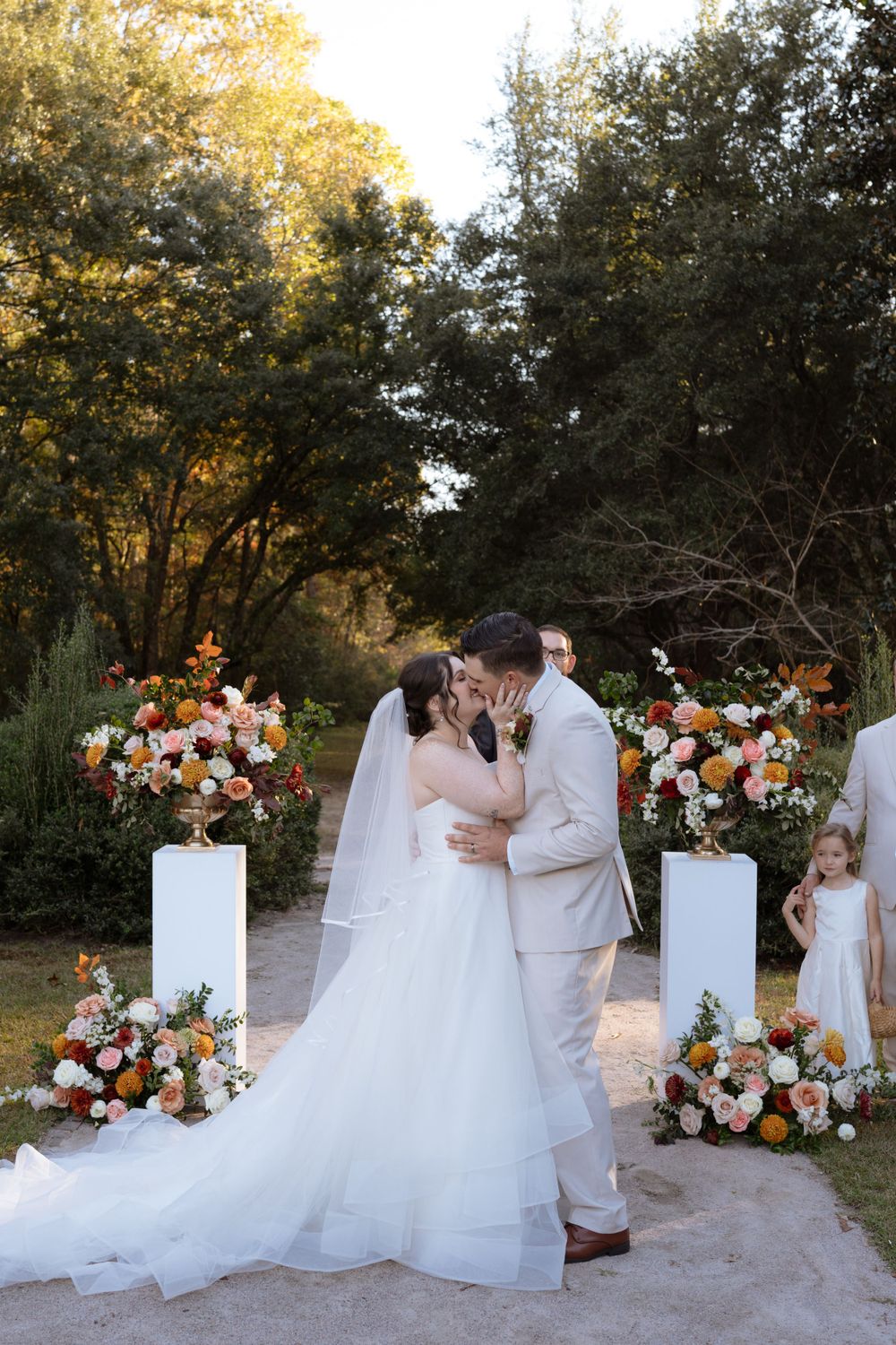Outdoor wedding ceremony with beautiful floral arrangements and white pedestals at sunset.