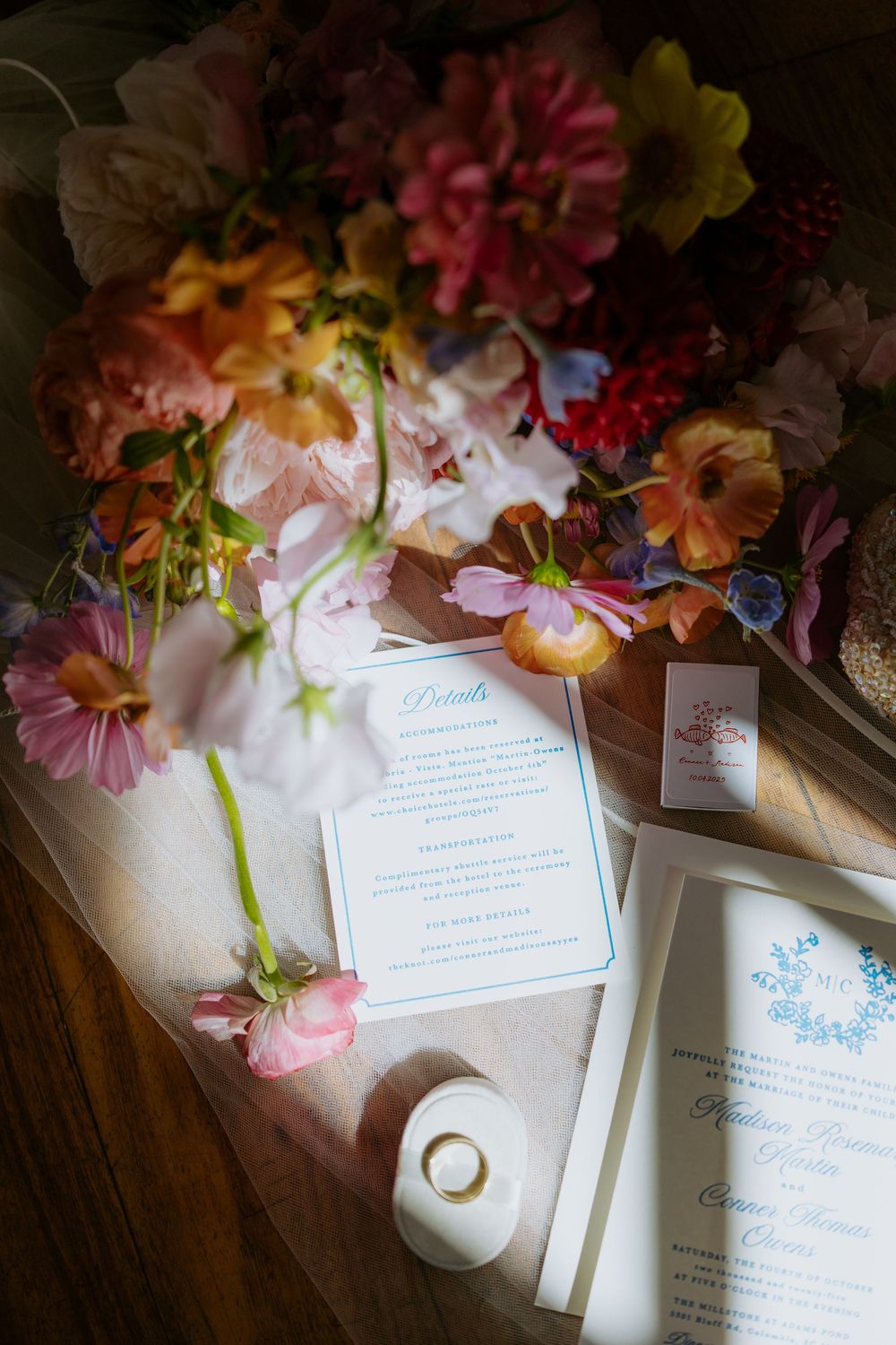 Wedding invitations decorated with colorful spring flowers and delicate paper details lay arranged on a wooden surface.