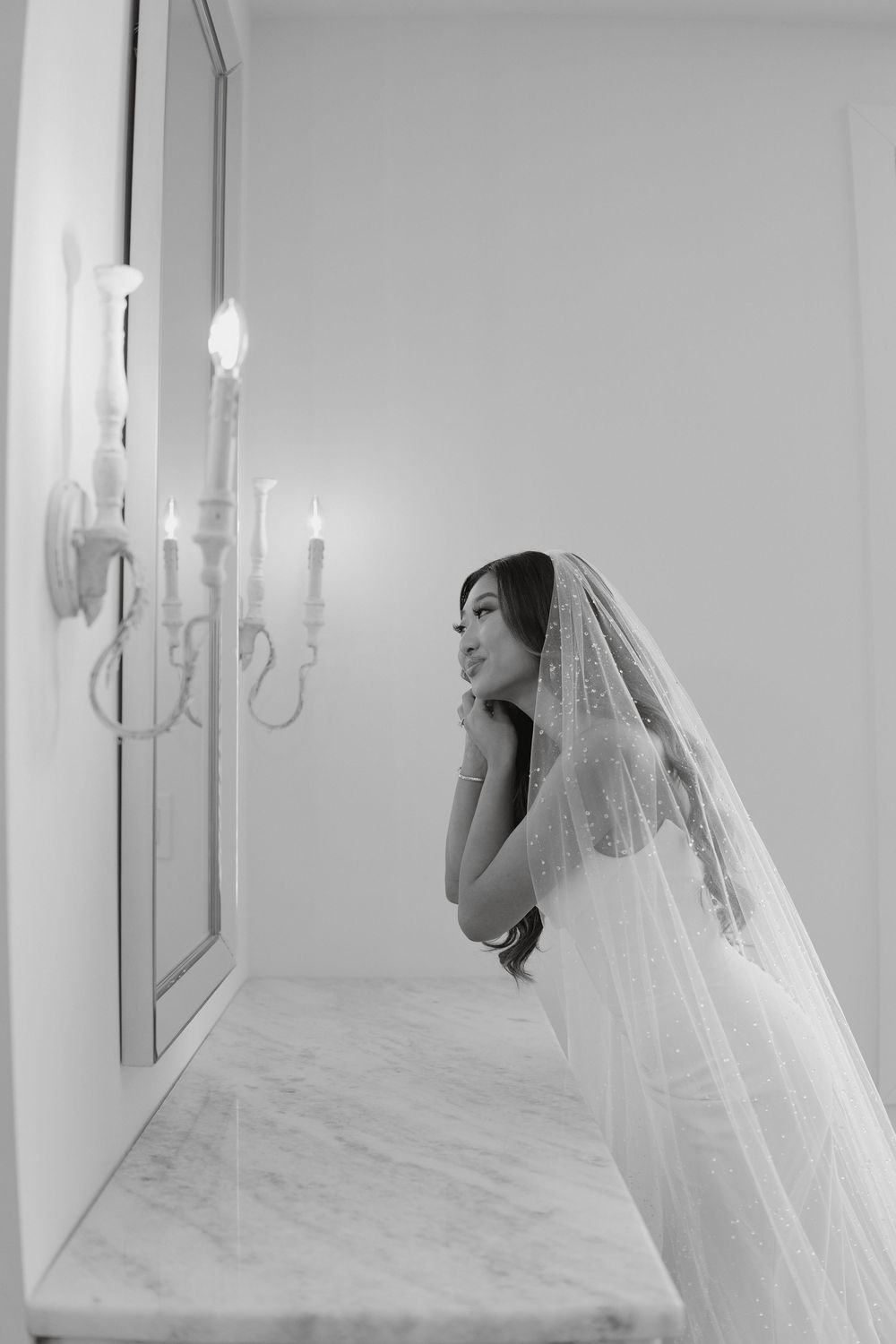 A bride leans over a marble surface near an elegant candelabra in a minimalist setting.