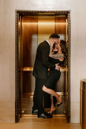 A romantic embrace in a golden-lit elevator with an ornate frame.