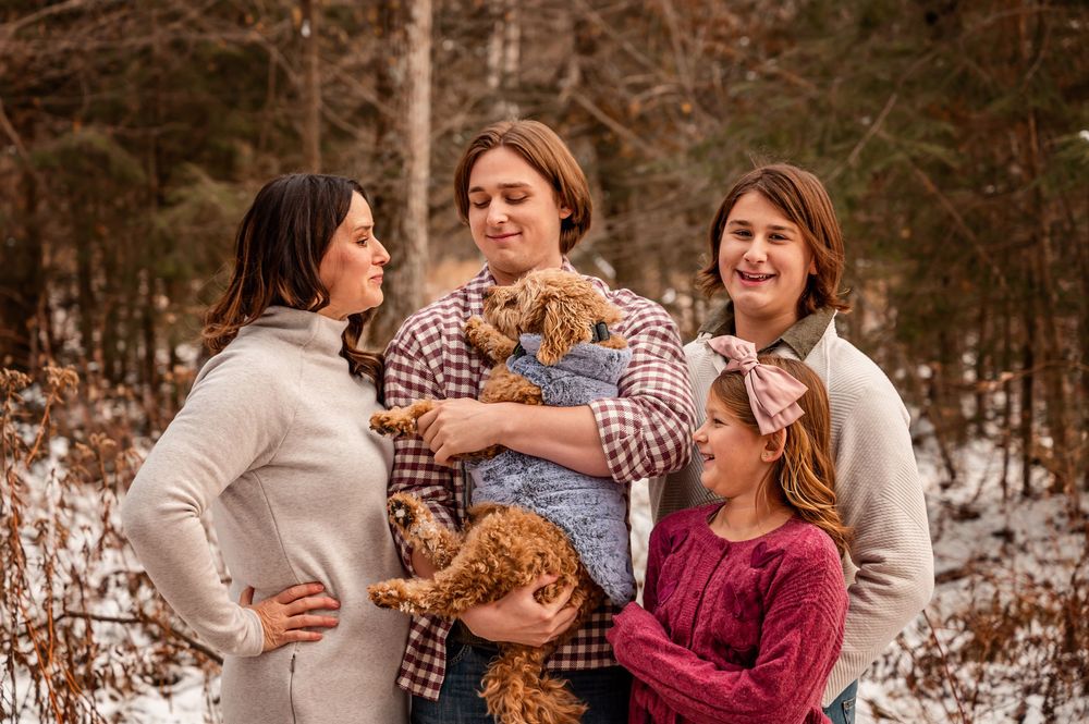 A family in coordinated winter outfits poses together in a snowy forest setting during a photo session.