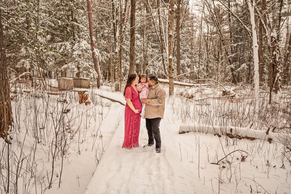 People walk through a snowy winter forest landscape with bare trees and white ground cover.