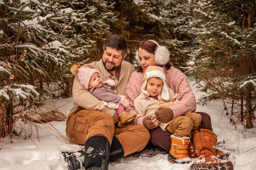 Family enjoying a winter photoshoot together in the snowy forest wearing coordinating brown and pink outfits.