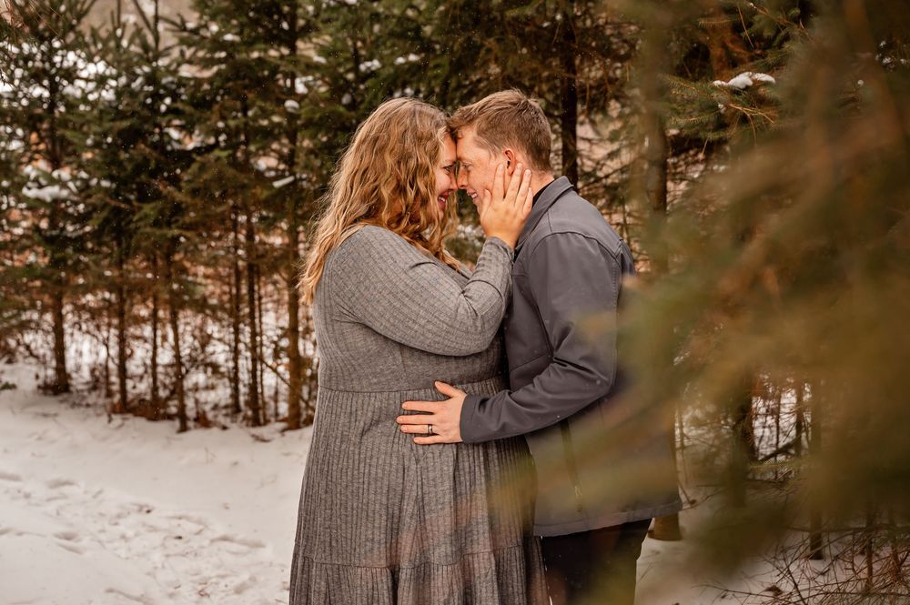 Couple embraces in snowy forest setting during winter photoshoot.