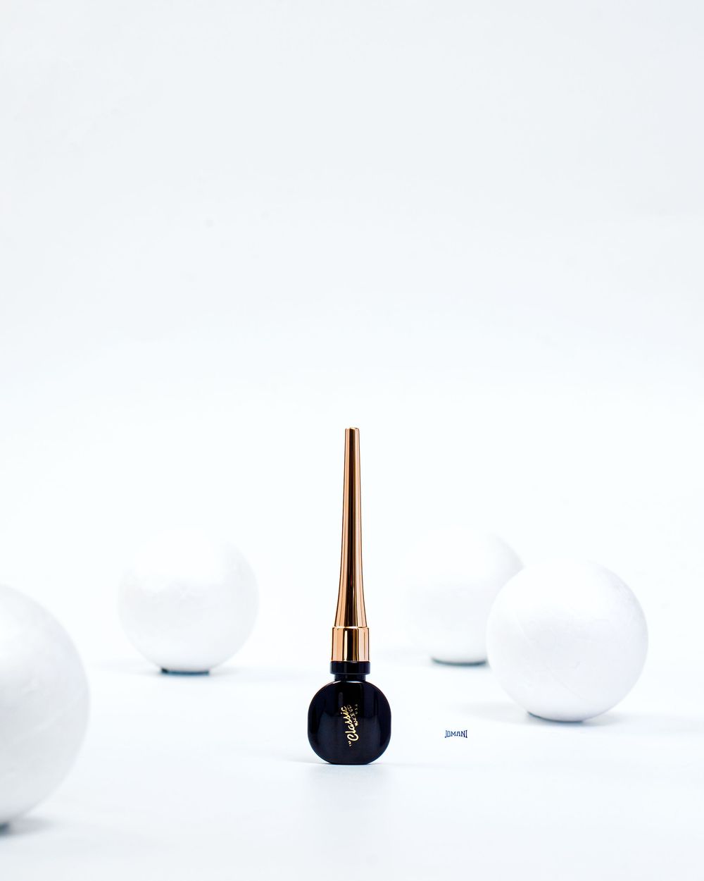 YSL black nail polish bottle with gold spike cap surrounded by white spheres on white background.