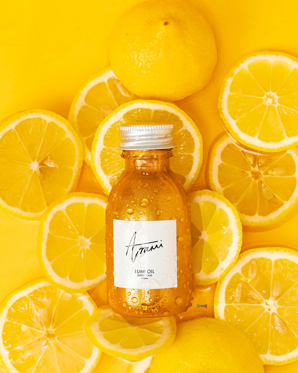 Golden body oil bottle by Amari surrounded by fresh sliced lemons on vibrant yellow background.