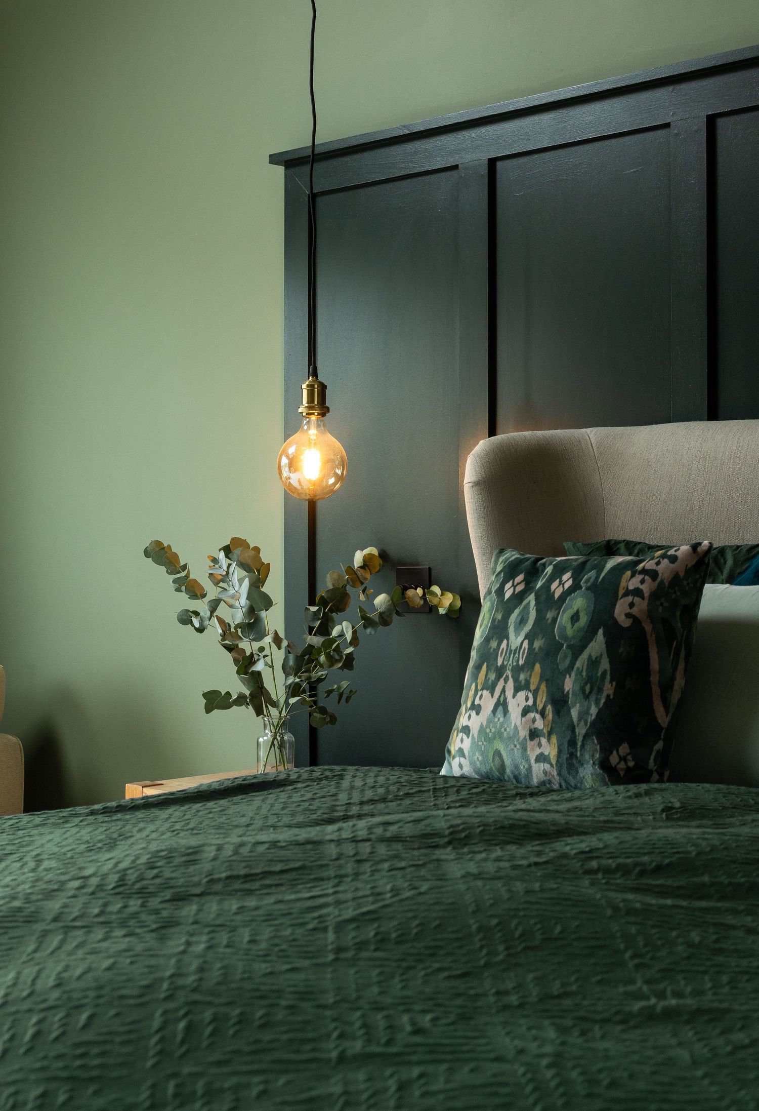 Dark green panelled bedroom with pendant light and patterned cushions, stylish interior design photography