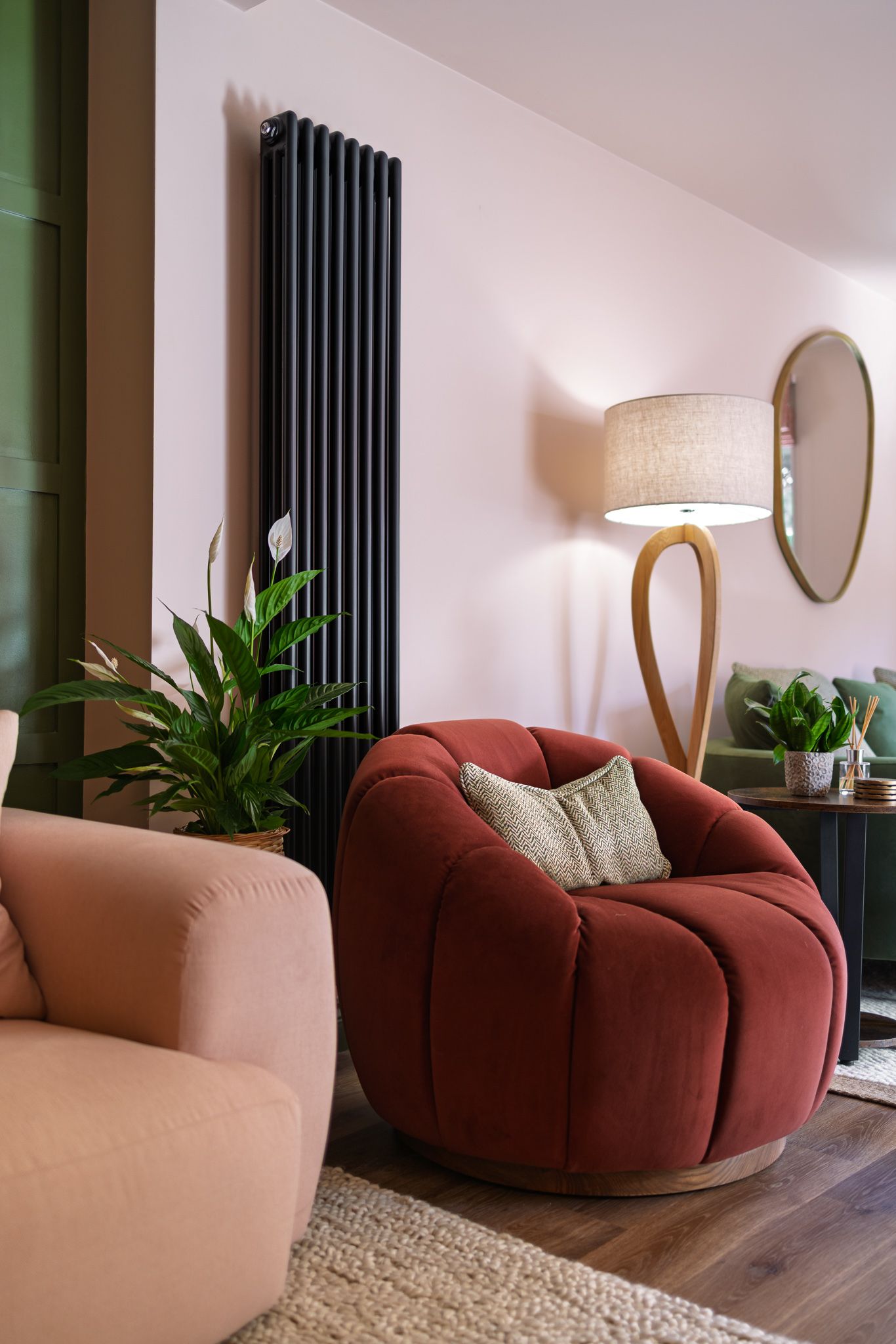 Stylish living room with curved pink and burgundy sofa, black radiator, round mirror and houseplants, interior design photography