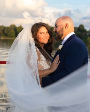 Romantic waterfront wedding portraits with flowing veil in soft sunset light.