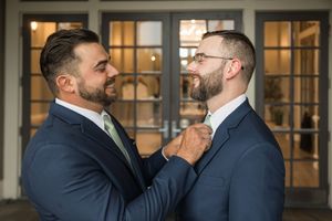 Two people in navy suits share a close moment during formal event preparations.