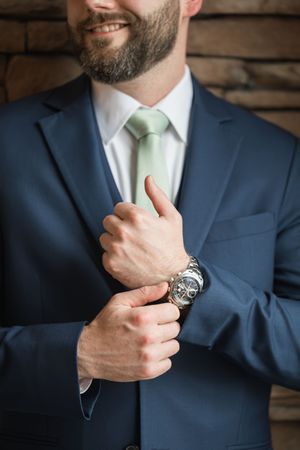 Close-up of a navy suit with mint green tie and silver watch details.