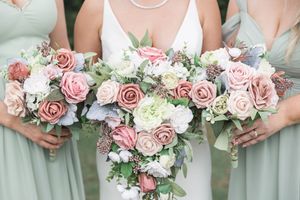 Bridesmaids holding pink and white rose bouquets with greenery.