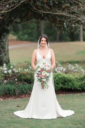 Bride in white wedding dress holding pink and white floral bouquet in garden setting.