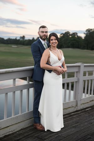 Newlyweds posing on wooden deck during sunset at golf course.