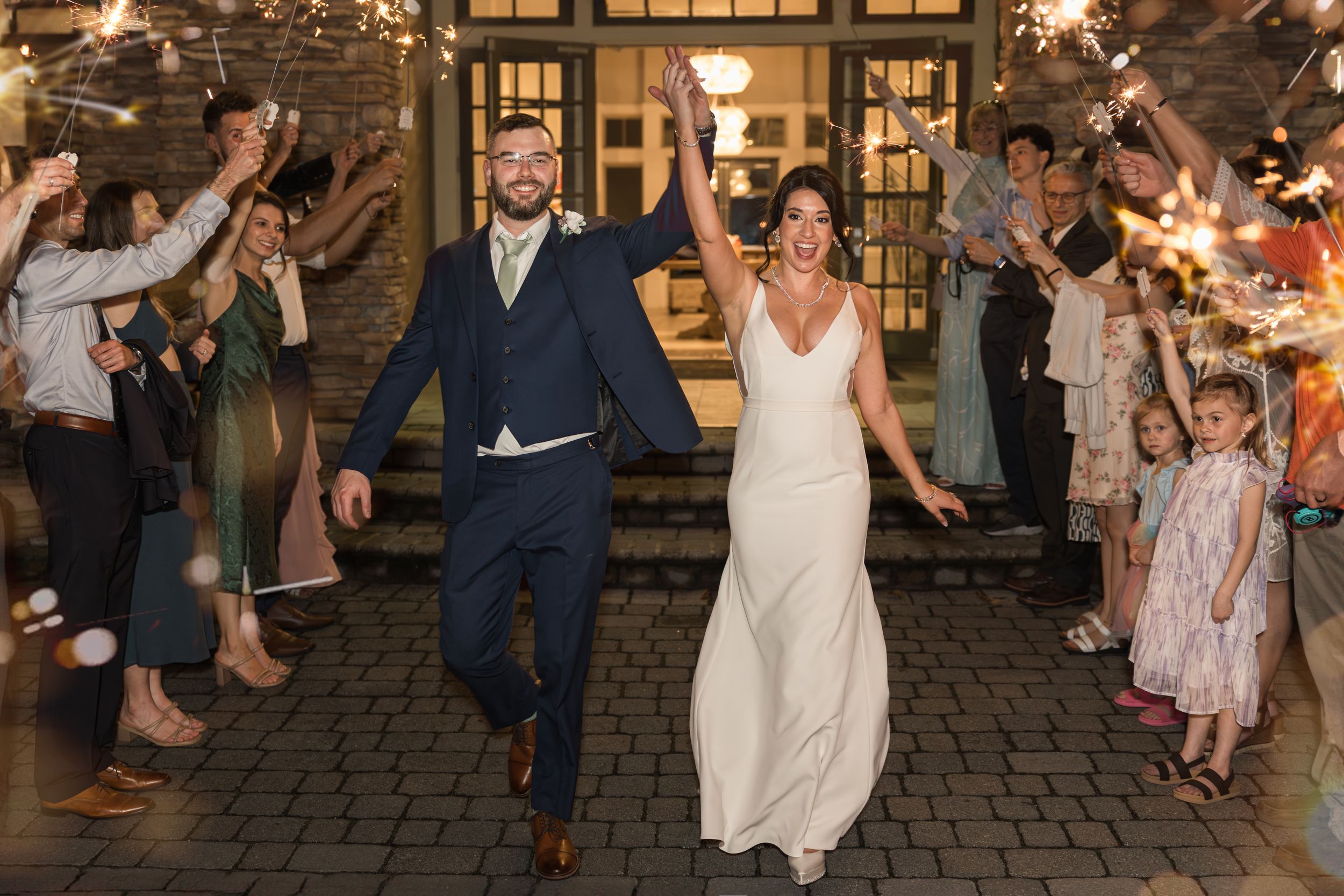 Wedding couple and guests celebrating with sparklers outside venue at night.