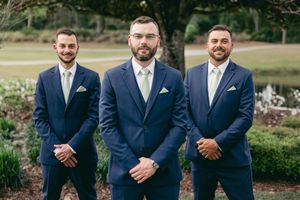 Groomsmen in navy blue suits and light colored ties standing together outdoors.