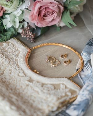 Wedding accessories including pink roses, jewelry, and lace details arranged on a neutral surface.
