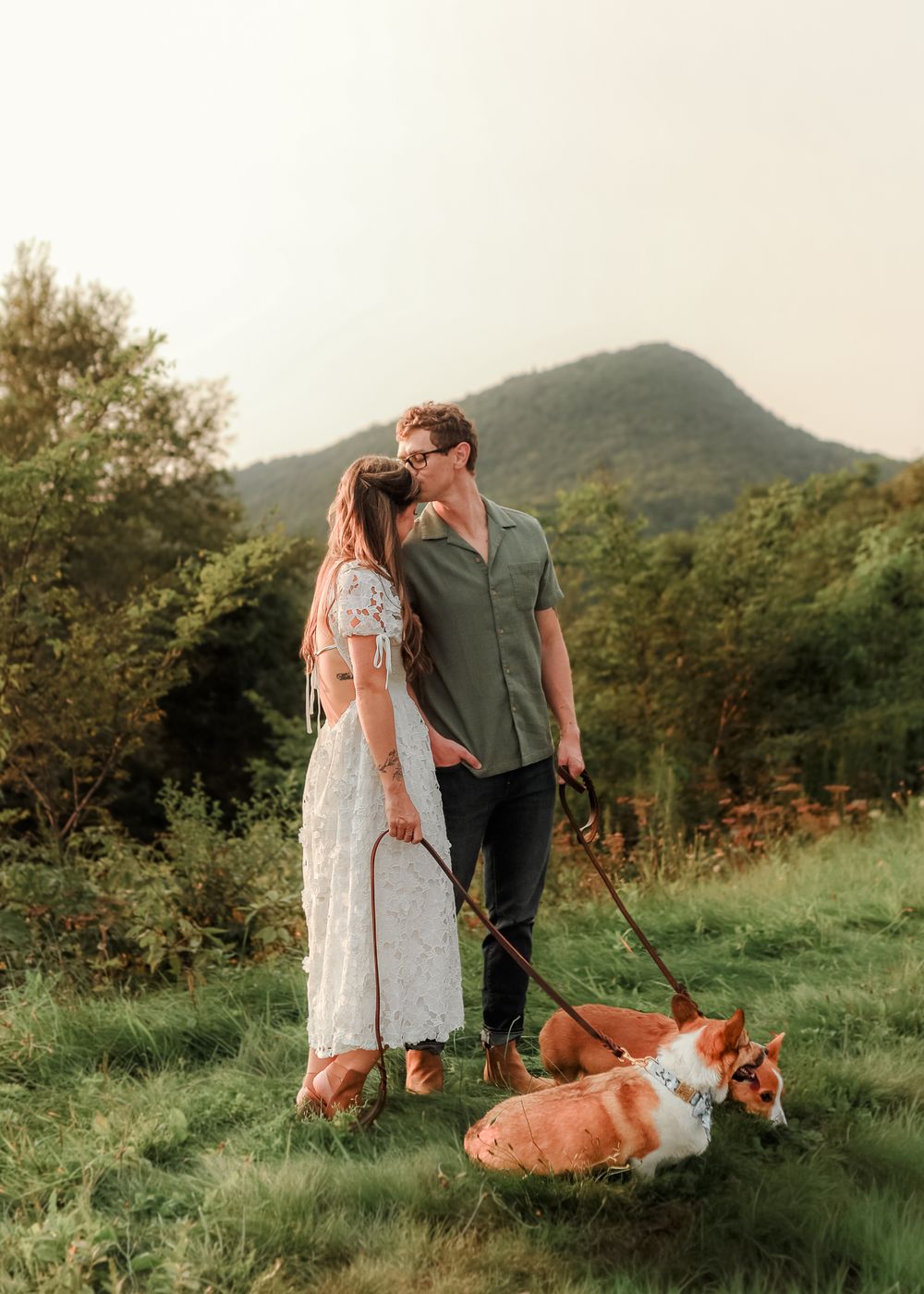 A couple walking their two ginger dogs on a scenic hillside during golden hour.