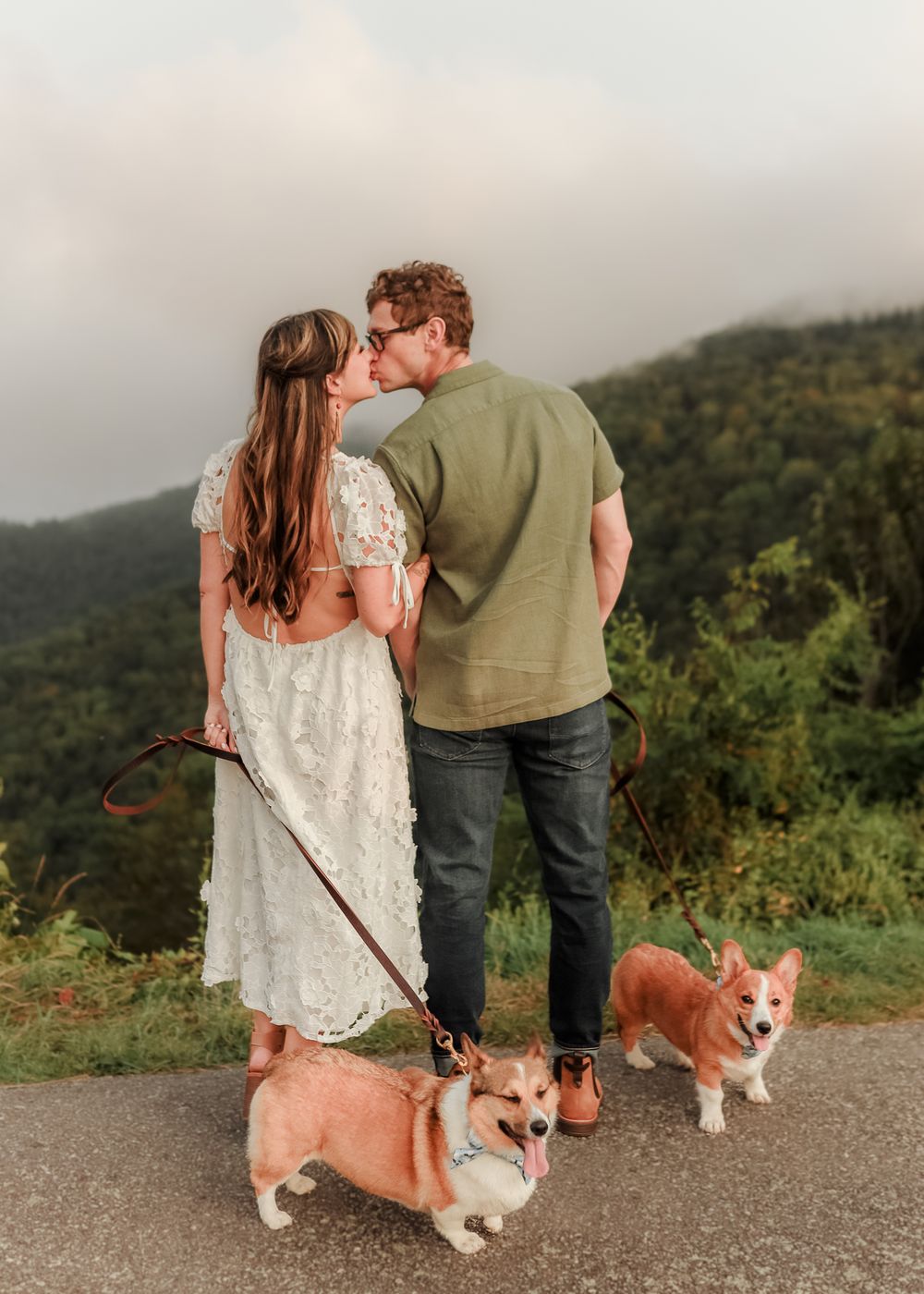 A couple shares romantic moments with their corgi dog while hiking along a misty mountain trail.