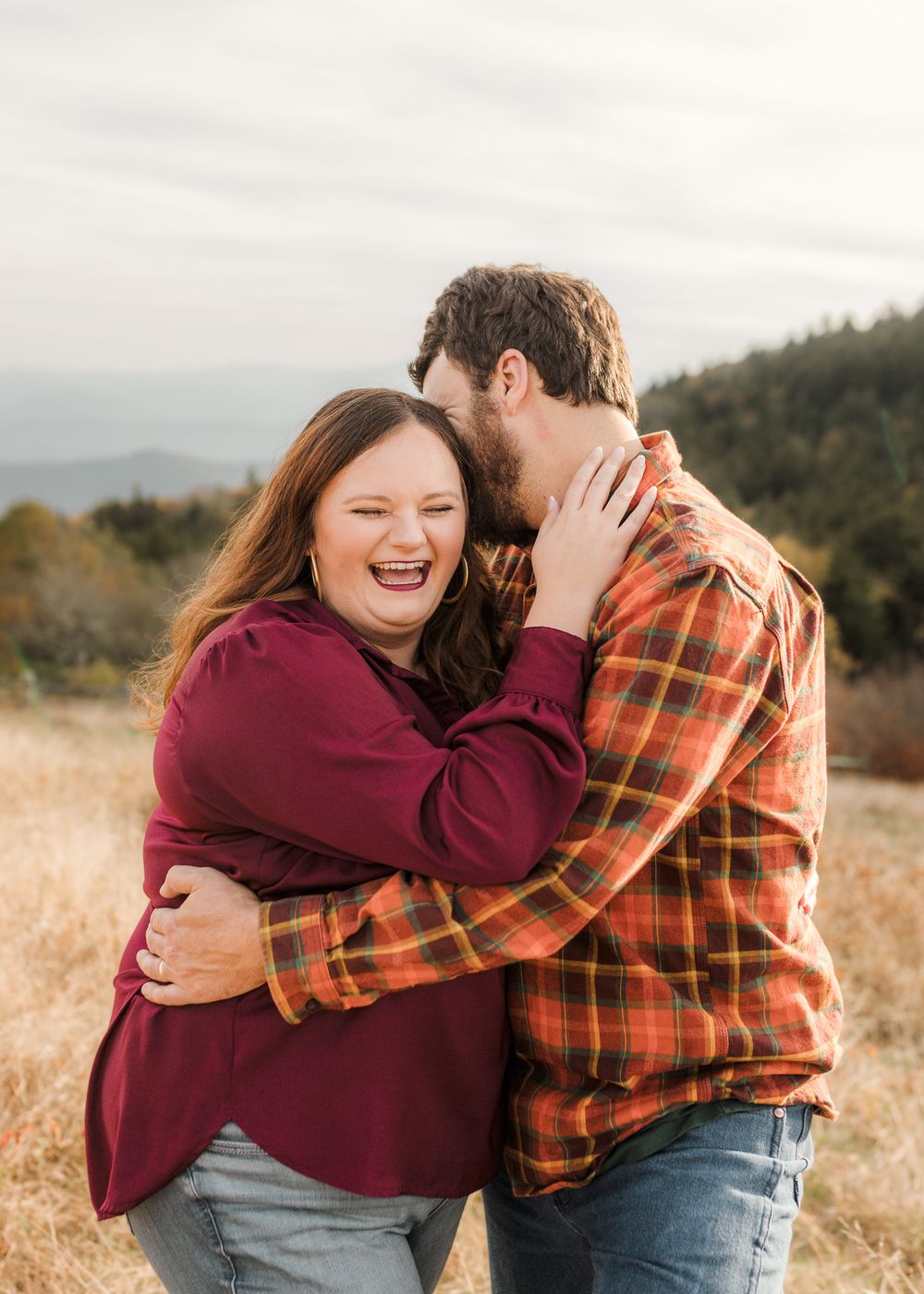 A couple in burgundy and plaid share joyful embraces in a golden autumn field at sunset.
