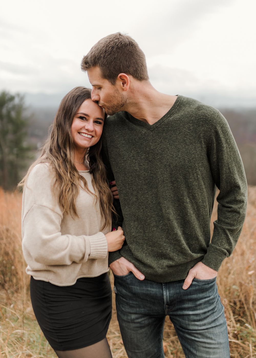 A couple in casual sweaters embraces while standing in a golden field during autumn.