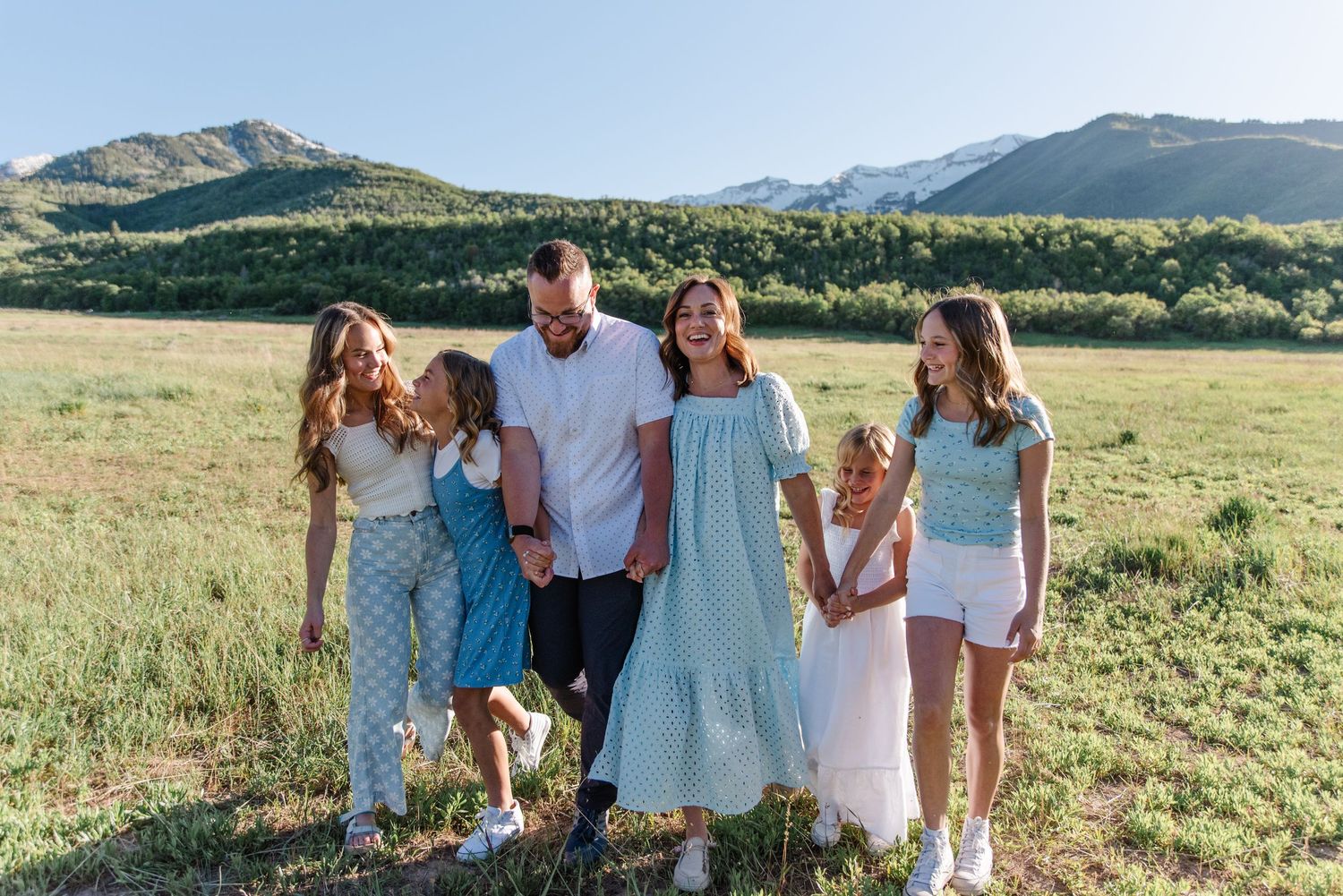 Family standing together outdoors in a meadow with mountain backdrop at sunset.