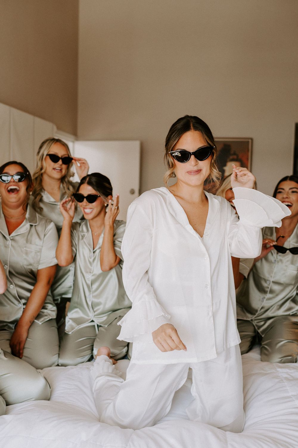 Wedding party in matching pajamas having fun with sunglasses on a bed.