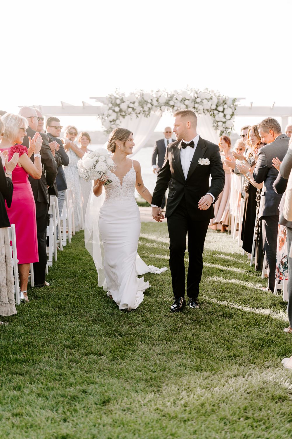 Newlyweds walk down the aisle as guests celebrate under a floral arch.